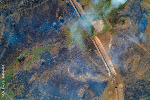 Canvas-taulu Aerial photograph of a landscape after a fire, featuring large plumes of smoke and scorched earth