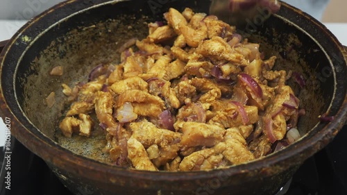 Pieces of chicken fillet with onion marinated in soy sauce and spices are fried in a frying pan. Medium shot.