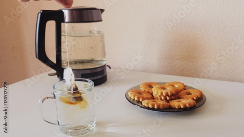 Tea is brewed from a tea bag in a white cup on a table with sweets. Medium shot.
