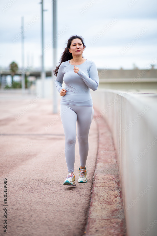 Fototapeta premium Focused Asian woman jogging outdoors in full-body grey active wear