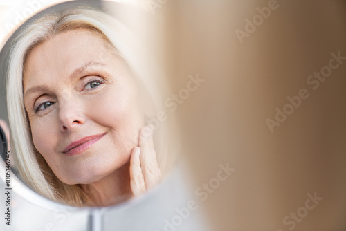 Beauty, reflection and mirror with aged woman in bathroom for morning routine, makeup grooming. Self care cosmetics foundation glow with mature person in home for cosmetology, shine hygiene