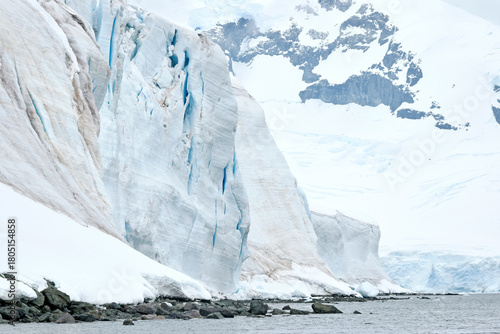 A mountain of snow and ice shows teal blue crevasses that will cause breaks and as chunks of ice fall away, will create icebergs, in Antarctica.