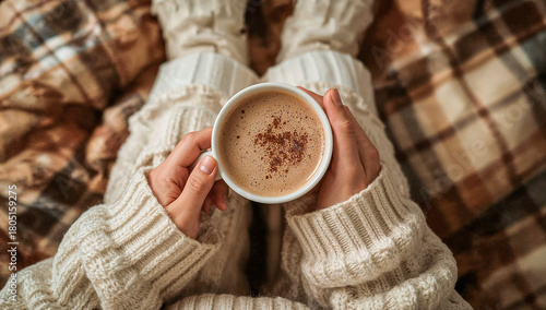 Cropped view of a woman wearing knitted winter warm socks and comfortable pajamas, holding a cup of hot cocoa with whipped cream and chocolate sprinkles. Cozy time. Top view