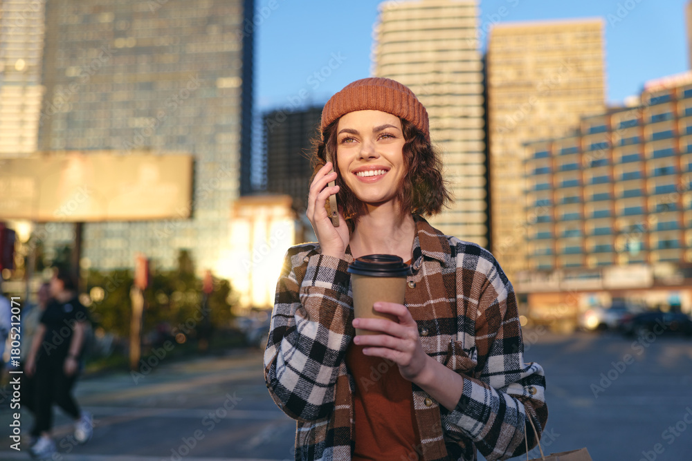 Fototapeta premium woman holding coffee and phone in urban street, smile in golden hour glow, candid lifestyle portrait emphasizing authenticity, mindful living and emotional storytelling in city scene