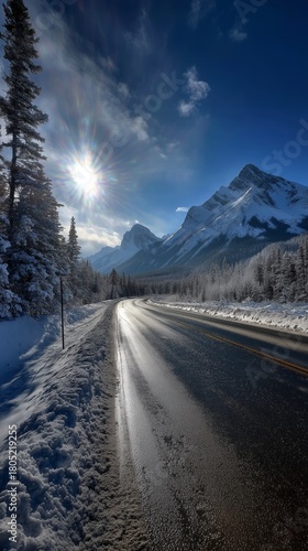 Snow-covered Road Surrounded by Tall Trees and Mountains on a Sunny Winter Day