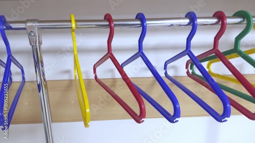 Empty colorful plastic clothes hangers on a metal rod.