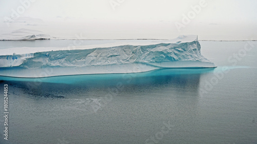 Water, ice and light make an iceberg appear to be pouring teal dye into the water, in Antarctica.