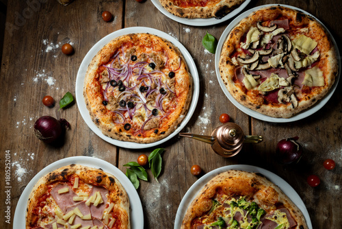 Pizzas aus dem Steinofen mit Gemüse, Brokkoli, Salami, Tomate, von oben fotografiert, mit Tomaten, Basilikum und Mehl auf dem Holztisch