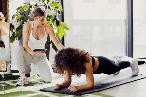 A fitness trainer is coaching a girl in the gym, guiding her and explaining proper form during exercises.
