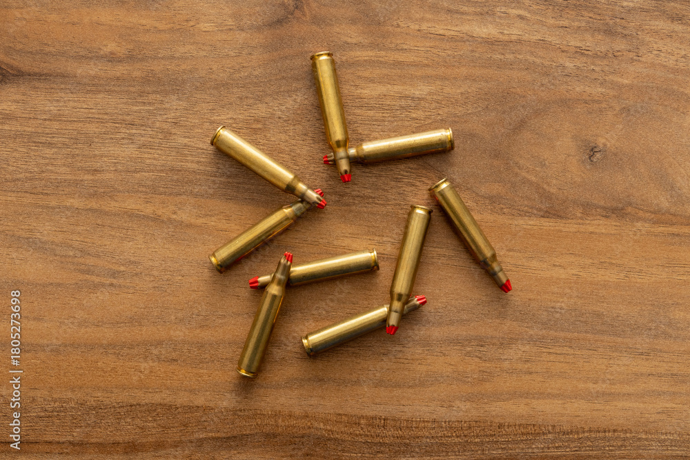 Arrangement of cartridges fanned across a wooden tabletop photographed from above to emphasize brass tones, repetition and conceptual tension between object pattern and thematic meaning.