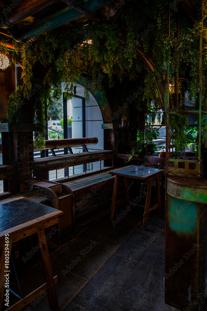 Obraz premium Atmospheric industrial-style café corner in Tel Aviv, Israel, featuring rustic metal elements, hanging greenery, wooden tables, and a moody urban interior design perfect for background or life style