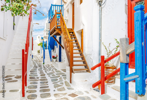Fototapeta Naklejka Na Ścianę i Meble -  A whitewashed alley with colorful red and blue accents leads to a small chapel with bell tower, in the old town of Mykonos, Greece.