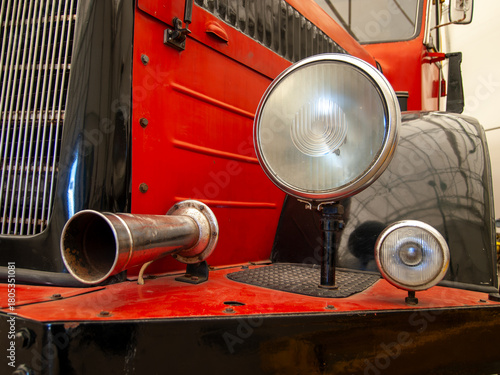 Close-up of vintage vehicle details with headlights, horn and grille in red and black colors, showing classic mechanical design