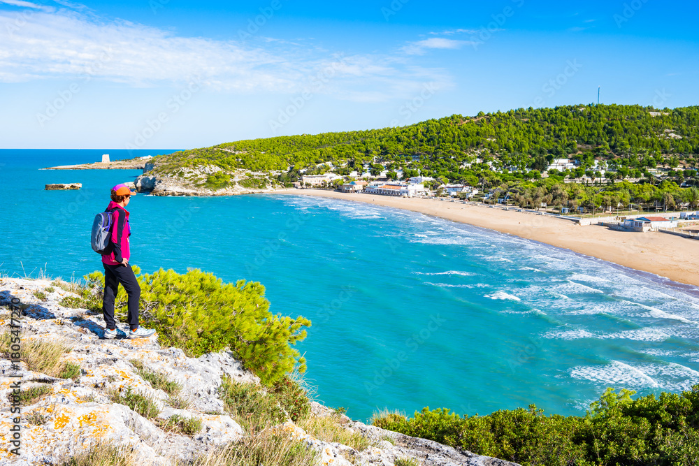 Obraz premium Female tourist at scenic viewpoint overlooking the Adriatic coast and golden beach near Peschici, Apulia, Italy