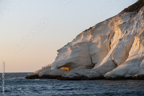 massive white chalk cliffs of Rosh HaNikra dramatically meet the dark blue Mediterranean Sea at sunset.  layered rock captures the warm, golden light