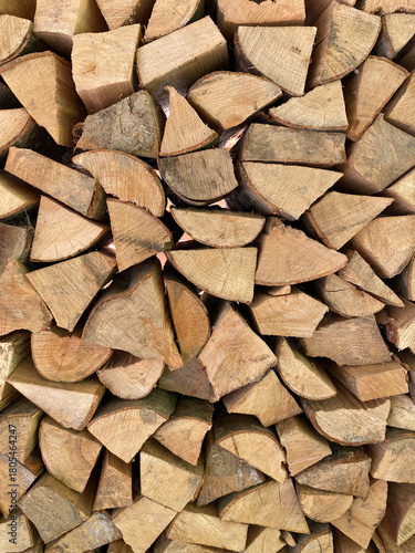 A close-up, full-frame texture of neatly stacked, split firewood. The seasoned logs form a dense, rustic background and geometric pattern perfect for themes of winter, warmth, and natural energy