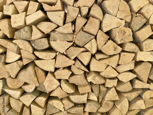 A close-up, full-frame texture of neatly stacked, split firewood. The seasoned logs form a dense, rustic background and geometric pattern perfect for themes of winter, warmth, and natural energy