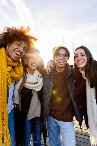 Four cheerful young multi-ethnic friends are hugging and laughing together during a sunny winter day