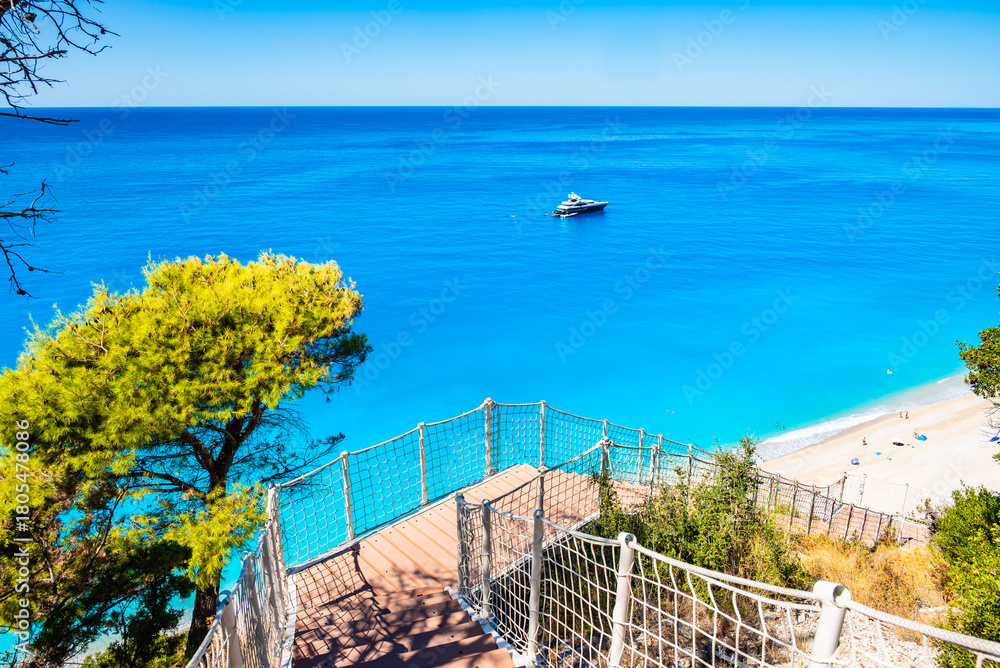 Fototapeta premium Path with stairs to amazing Egremni beach with tuquoise water and anchored boat, Lefkada island, Greece