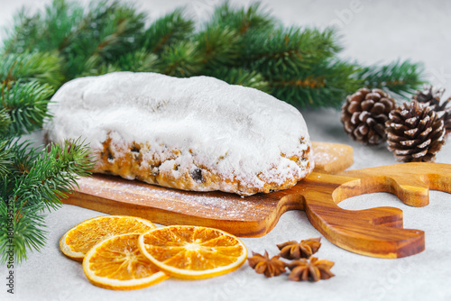 Traditional Christmas Stollen, sweet fruit loaf with sugar icing on wooden board and festive decor