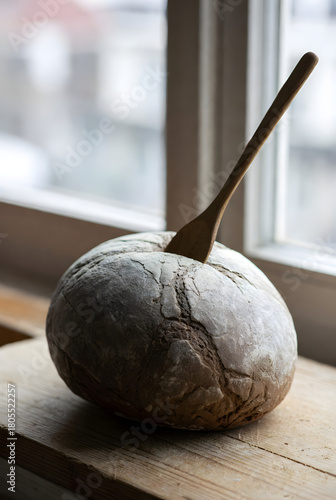 Rustic round loaf of bread with wooden spoon on windowsill