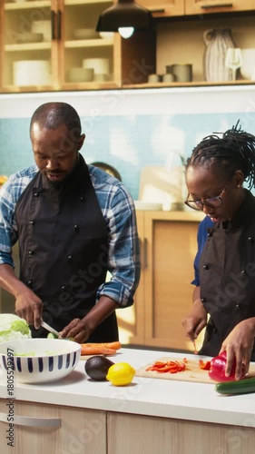 Vertical Video Black young lovers chopping veggies and preparing ingredients on the cutting board, cooking together. Couple cutting organic vegetables for a salad bowl, relaxed fun energy at home