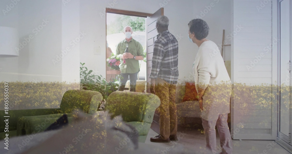Fototapeta premium Holding bouquet, masked visitor in green shirt presenting package at front door, residents masked