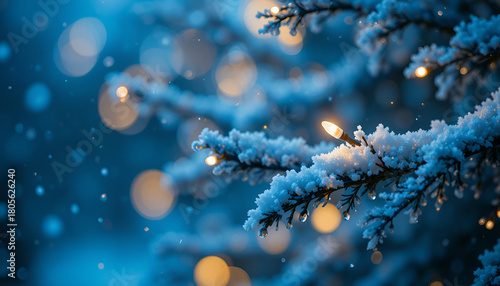 Snowy christmas tree branch illuminated with warm lights against a blurred blue bokeh background