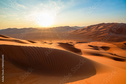 Rub' al-Khali (Empty Quarter) desert in Thumrayt, Dhofar, Oman, presenting sprawling orange sand dunes and a small settlement at the foot of distant hills under a clear morning sky