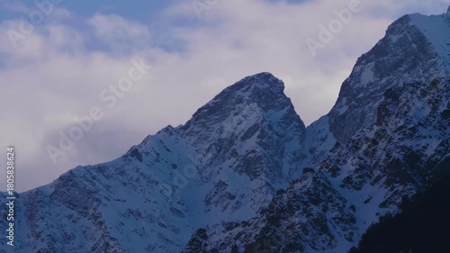 A view of the snow covered peaks of the North Caucasus mountain range in Russia. The dramatic landscape features rugged, rocky mountains blanketed in snow under a cloudy sky, capturing the serene and 
