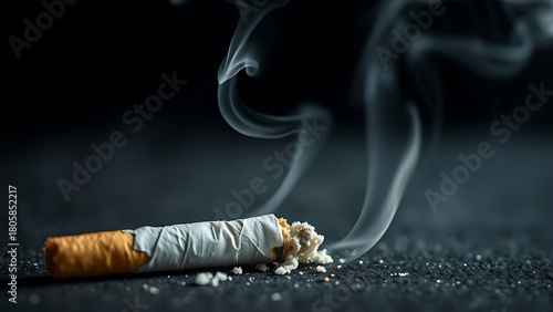 Crushed cigarette with rising smoke on a dark surface, symbolic concept.