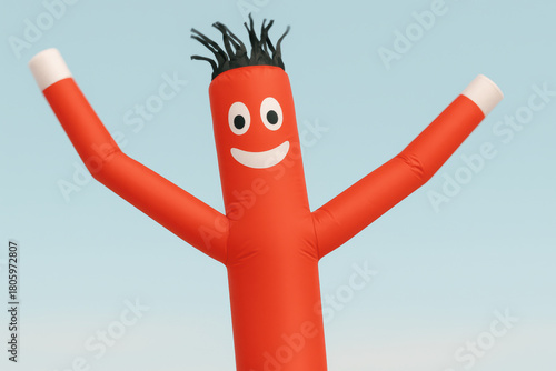 Cheerful red inflatable tube man with smiling face and raised arms against clear blue sky, promoting fun and excitement outdoors