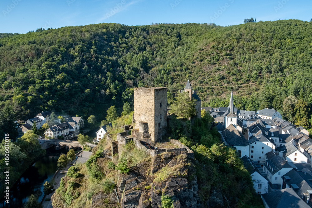 Naklejka premium Esch-sur-Sure, Wiltz, Grand-Duche de Luxembourg, September 07, 2025, Historic fortress panorama, Mountain stronghold overlooking trees, Castle perched above lush forest and flowing river