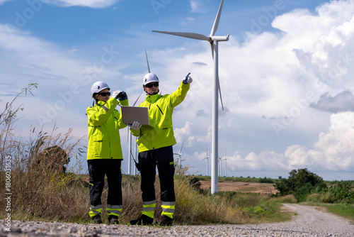 Workers assess wind turbines while conducting a site evaluation in a renewable energy field under a blue sky