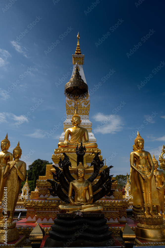 Fototapeta premium Phra That Phanom stupa with golden Buddha statues and vibrant naga serpents, showcasing ornate Thai architecture, sacred temple art, and spiritual heritage under a bright blue sky