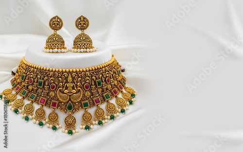 Elegant traditional Indian antique gold temple jewelry choker necklace set, gemstones and hanging pearls on white silk background