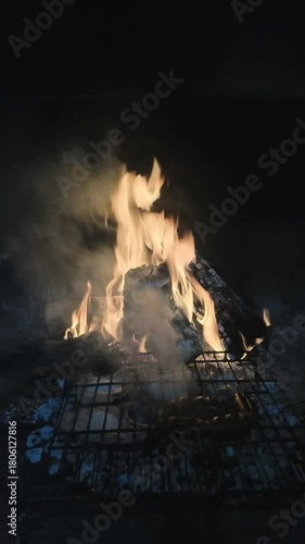 Meat is being cooked on grills, over the embers of a bonfire, preparing dinner in a barbecue area.