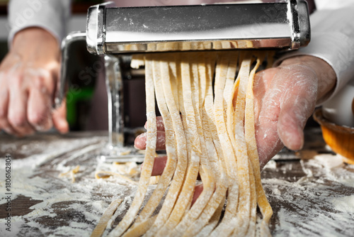 Caucasian female hands making fettuccine noodles using mechanical pasta machine
