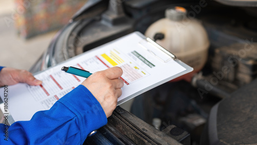 Action of a car service technician is checking on vehicle inspection checklist form during perform the maintenance job. Close-up and selective focus.