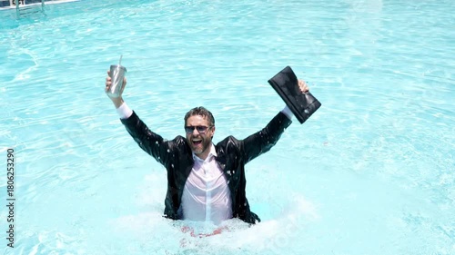 Funny businessman in suit working with computer on the sea beach. Summer holiday, outdoor and business travel concept. Crazy office worker. Man working on laptop computer sitting in cloth at poolside.