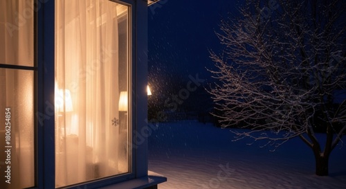 Cozy winter snowfall scene looking out the window at a snow covered tree glowing with inviting warm light creating a sense of peace and serenity