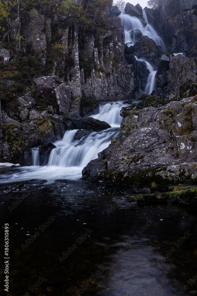 Obraz premium Waterfall tumbling over dark rocks into a still pool in Snowdonia