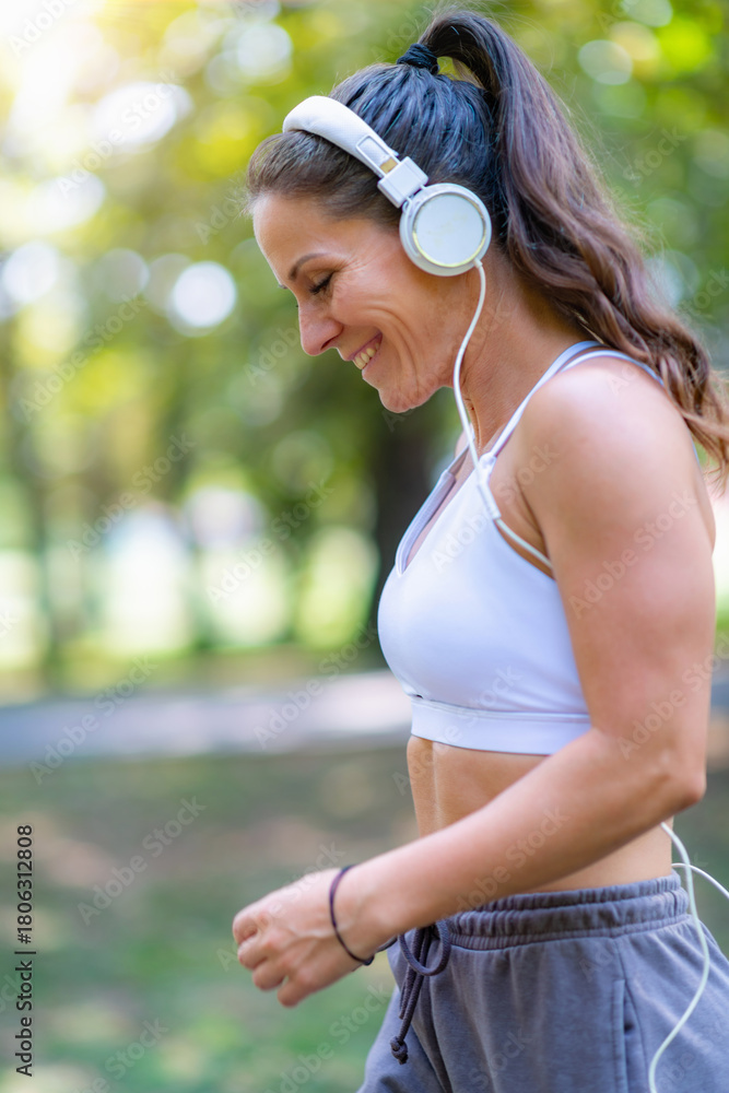 Fototapeta premium Woman walking outdoors in modern sports clothes and headphones, enjoying recreation and movement. Encourages active lifestyle and relaxation.
