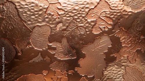 Close-up of an intricate embossed copper surface featuring various leaf patterns with a textured finish showcasing fine details in soft warm light representing artistry and craftsmanship in design.