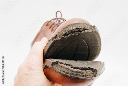 Worn out shoes held in hand showcasing damaged sole