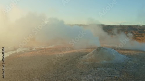 A wide shot of the famous Strokkur geyser erupting steam and hot water from a geothermal field in Iceland.