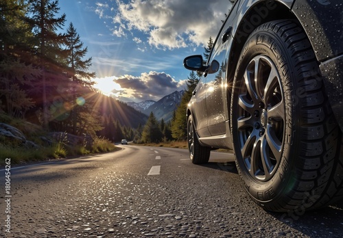 close-up of a car tire on a winding mountain road with golden sunlight and scenic landscape.