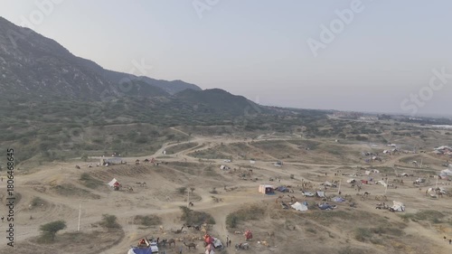 Shot of the Pushkar cattle fair ground showing camels and tents during the fair, with the Aravalli mountains in the background capturing the vibrant desert atmosphere.