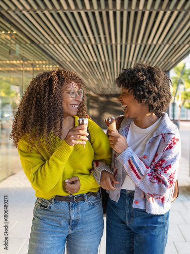 Two smiling women friends eating ice cream enjoying city walk