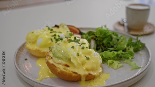 Delicious eggs benedict served on a plate with fresh greens and coffee in a cozy indoor restaurant setting.